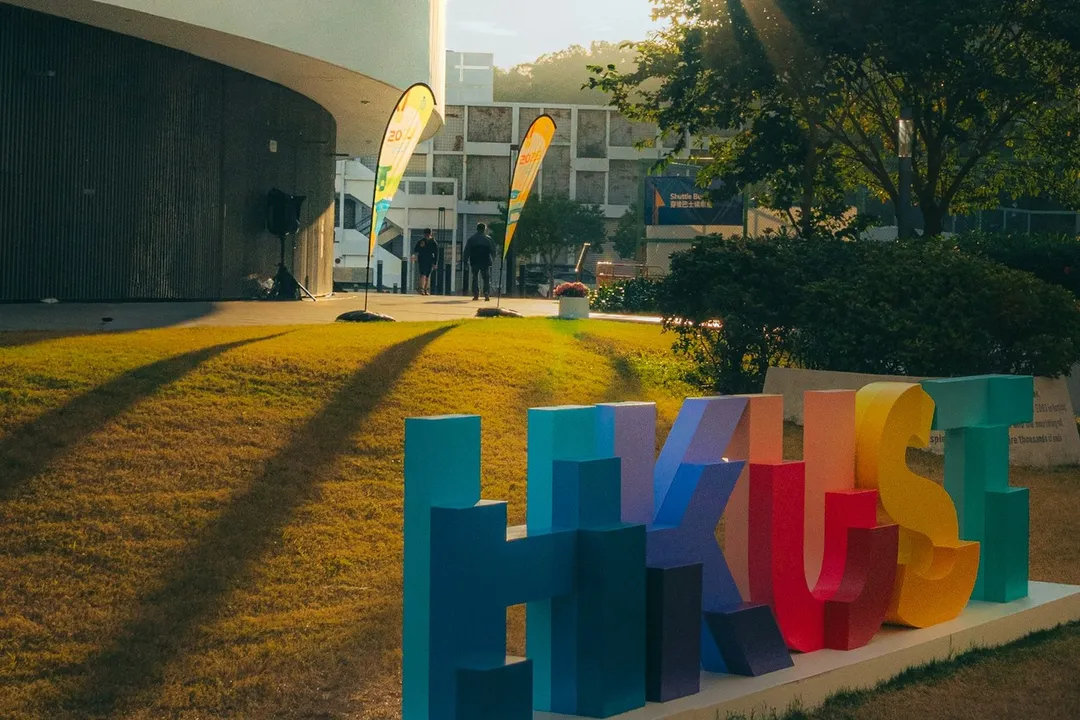 Colorful HKUST letter sign on the university lawn at sunset.